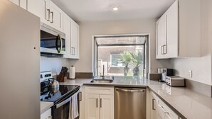 A modern kitchen with white cabinets, stainless steel appliances, and a window providing a view of the outside. - 1 Block to Beach/Restaurants/Bars, Remodeled, 2-Car Garage w/fee, Yard, Sleep 10 (San Diego)