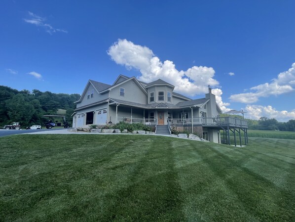 A large, two-story house with a wrap-around porch, a covered deck, and a well-maintained lawn.