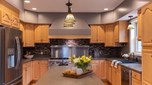 Una cocina moderna con armarios de madera, una isla central, electrodomésticos de acero inoxidable e iluminación decorativa.