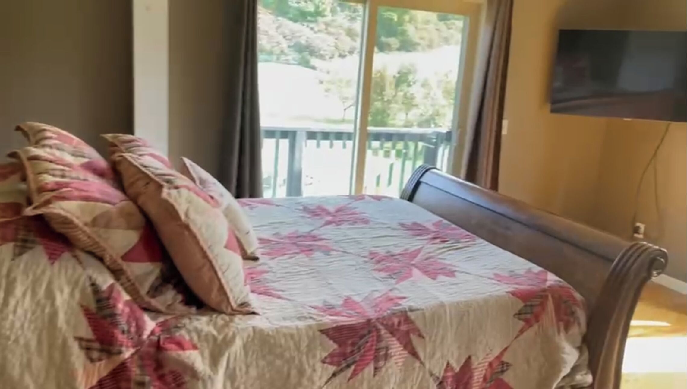 A bed with a floral bedspread and pillows, a wooden headboard, and a view of a balcony with a railing.