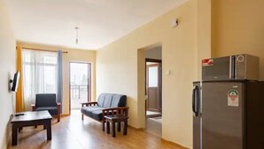 Un salon avec un canapé, une table basse, un réfrigérateur et une fenêtre avec des rideaux.