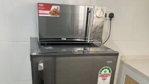 Ein Edelstahl-Kühlschrank mit integriertem Mikrowellenherd und einer kleinen Mülltonne daneben.