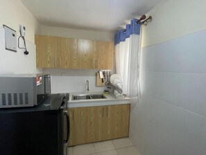 Uma cozinha compacta com armários de madeira, micro-ondas embutido, pia e janela com cortina.