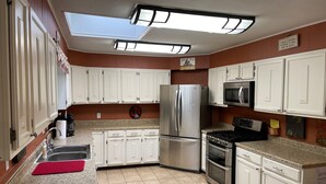 Una cocina con armarios blancos, electrodomésticos de acero inoxidable, un tapete rojo y un tragaluz.