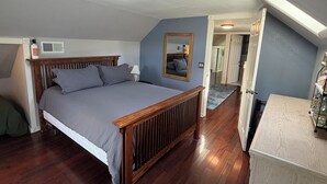 Un dormitorio con cama de madera, un espejo, un radiador y una puerta que da a otra habitación.