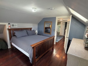 A bedroom with a wooden bed, a mirror, a radiator, and a door leading to another room.