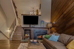 A living room with a fireplace, a sofa, a coffee table, and a TV mounted above the fireplace.