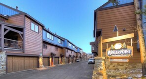 A street view of a residential area with wooden houses, a sign for 'Winterpoint,' and a stone wall with a lamp post.