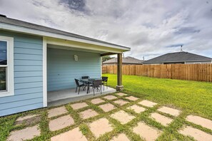 Une maison dotée d’un patio couvert comprenant une table et des chaises, une clôture en bois en arrière-plan et un ciel nuageux.