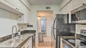Una cocina con armarios blancos, un fregadero de acero inoxidable, un refrigerador y una estufa.
