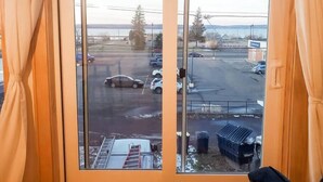 A view from a room with a large window overlooking a parking lot and a building across the street.