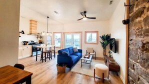 A spacious living area with a blue sofa, wooden dining table, and a kitchen in the background.