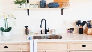 A kitchen with a sink, cabinets, and shelves with dishes and kitchenware.