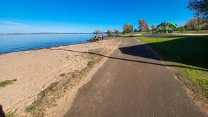 Un sentier pavé longe un parc au bord du lac, avec une aire de jeux et un bâtiment en arrière-plan.
