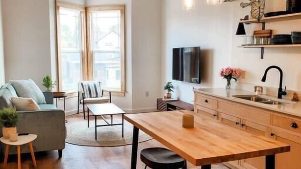 Une cuisine moderne avec une table en bois et des tabourets de bar, un ventilateur de plafond et des luminaires suspendus.