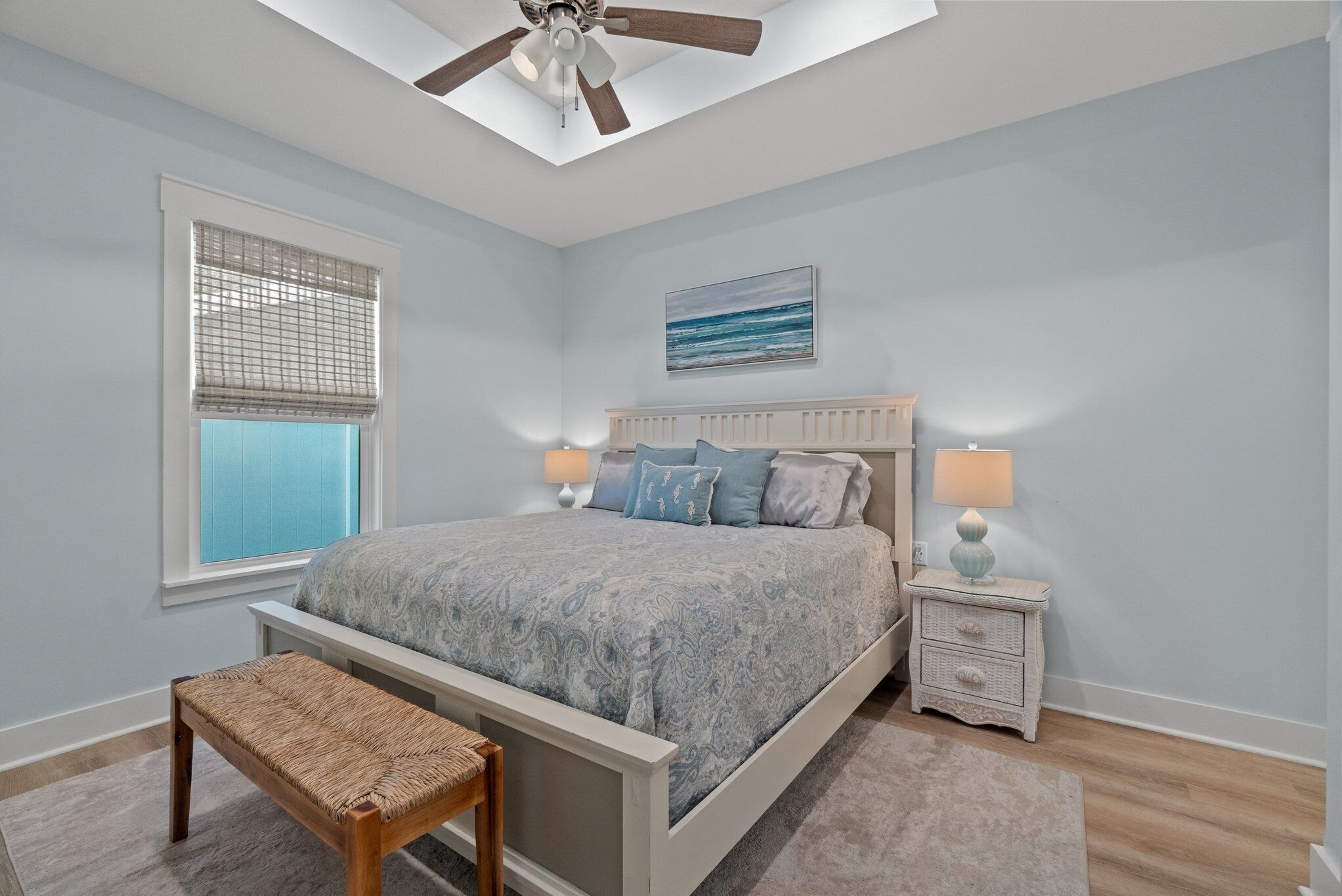 A bedroom with a bed, bedside tables, a bench, a ceiling fan, and a window with blinds.