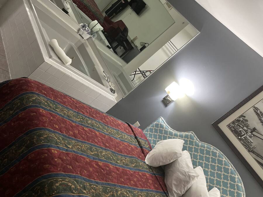 A hotel room with a large bed, a bathroom with a bathtub, and a mirror reflecting the room.