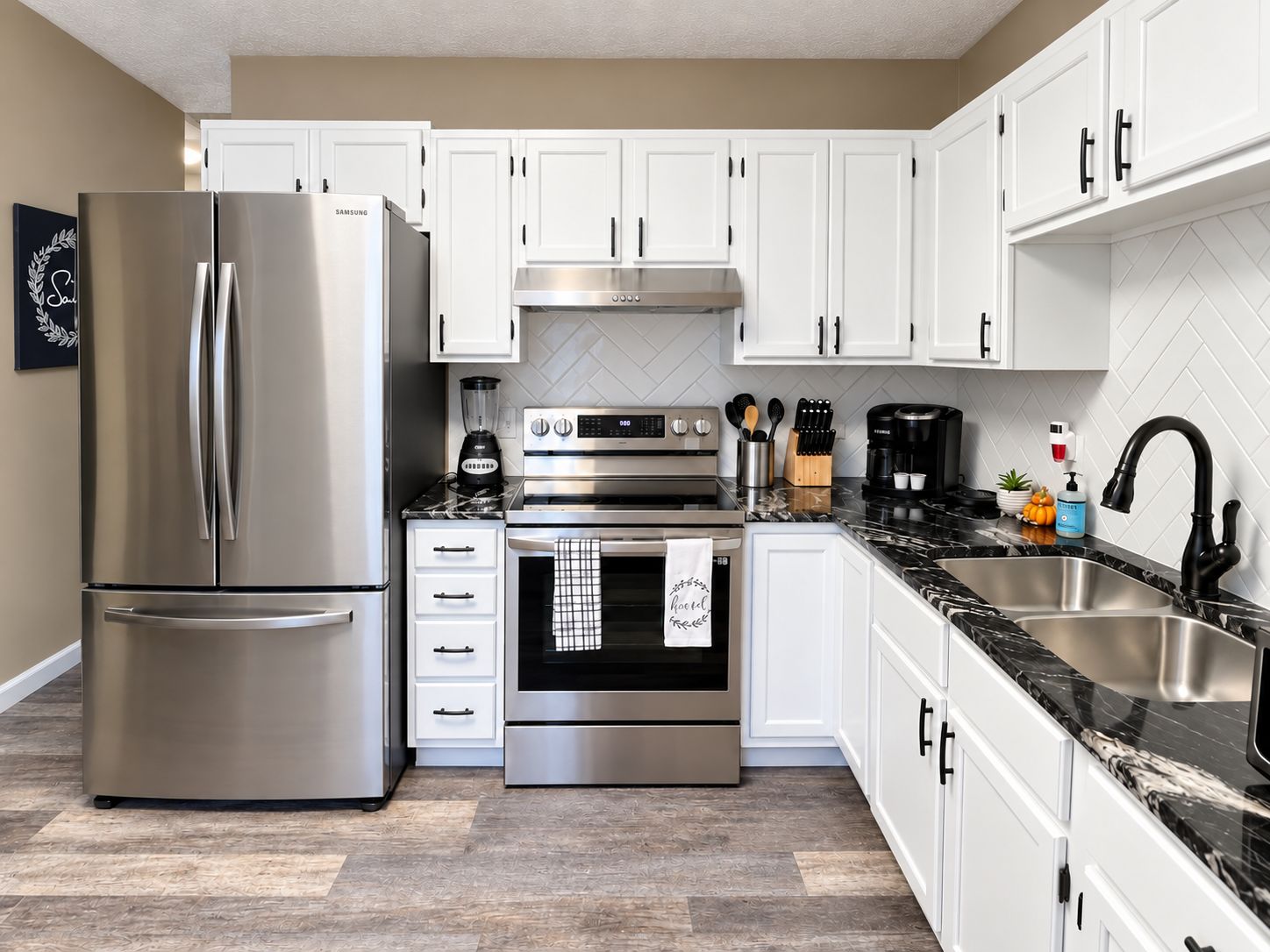 A modern kitchen with stainless steel appliances, white cabinetry, and a marble countertop.