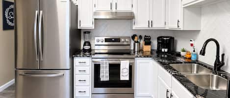A modern kitchen with stainless steel appliances, white cabinetry, and a marble countertop.
