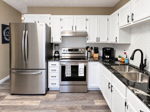 A modern kitchen with stainless steel appliances, white cabinetry, and a marble countertop.