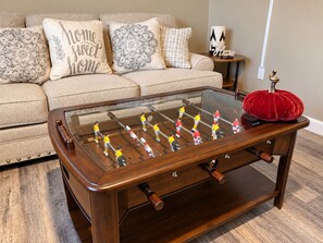 A foosball table with a glass top and wooden frame, placed on a wooden floor.