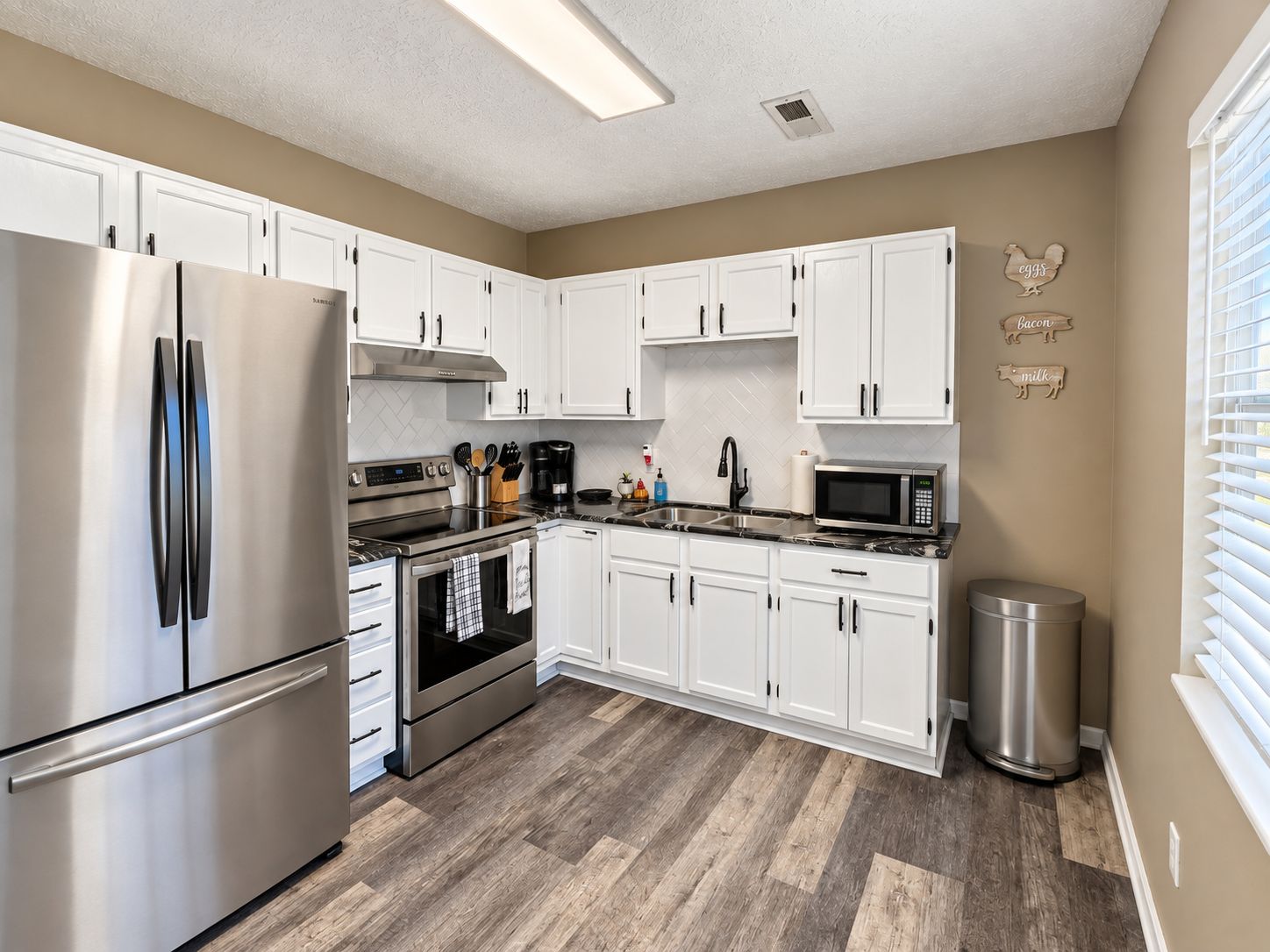 A modern kitchen with white cabinets, stainless steel appliances, and a herringbone wood floor.