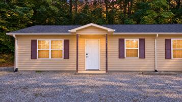 A single-story house with a front door, two windows with shutters, and a gravel driveway.