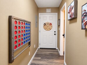 A hallway with a door, a wall-mounted game board, and two framed artworks.