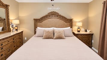 A bedroom with a large bed, wooden headboard, two bedside tables with lamps, a ceiling fan, and a mirror on the left wall.