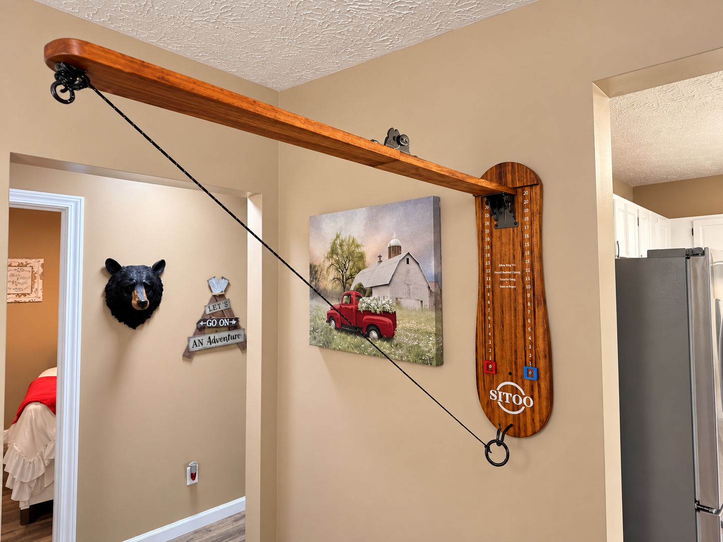 Une cuisine avec une étagère en bois soutenue par une poutre, un calendrier mural, une décoration représentant une tête d’ours et un tableau représentant un camion rouge.