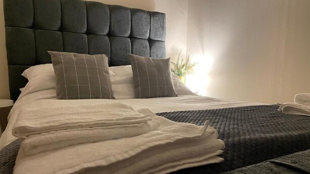 A neatly made bed with a dark headboard, white linens, and two pillows. - Taynuilt Guest House (Taynuilt)
