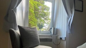 A corner room with a window, a radiator, and a chair. - Taynuilt Guest House (Taynuilt)