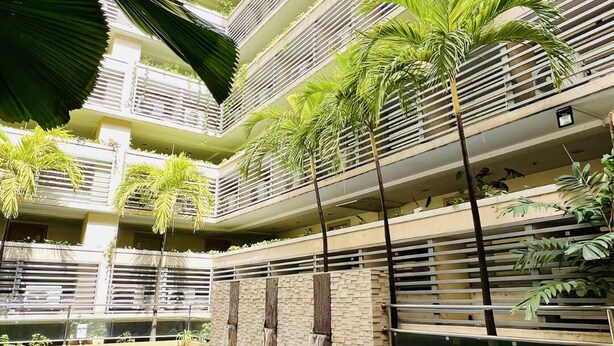 A multi-story building with a swimming pool, balconies with plants, and a wooden deck.