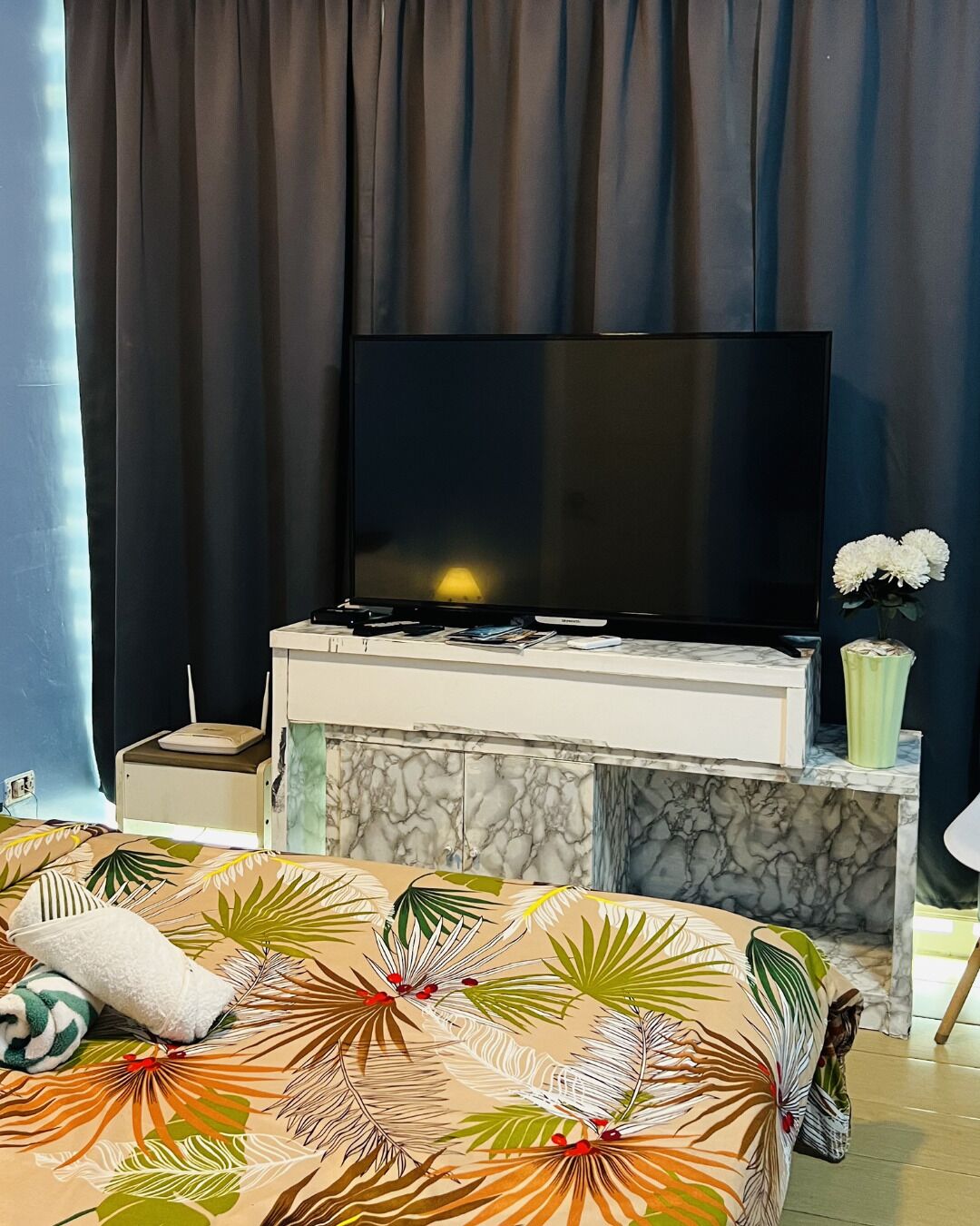 Habitación de hotel con cama, televisor de pantalla plana, consola de mármol, una mesita y un florero con flores.