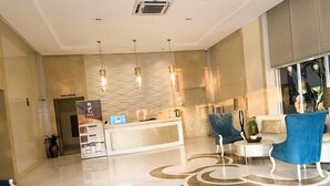 A hotel lobby with a reception desk, a blue chair, and a patterned floor.