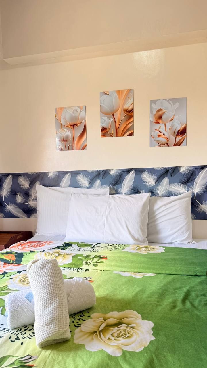 A bed with white pillows, a green floral bedspread, and three wall-mounted paintings of flowers.