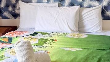 A bed with white pillows, a green floral bedspread, and three wall-mounted paintings of flowers.