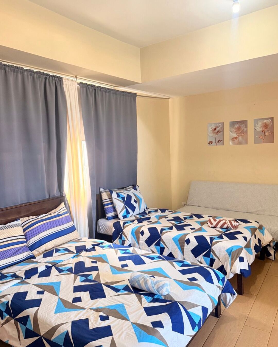 Un dormitorio con dos camas, una ventana con cortinas y una pared con tres cuadros enmarcados.