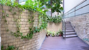 A brick wall with climbing plants, a wooden staircase, and potted plants.