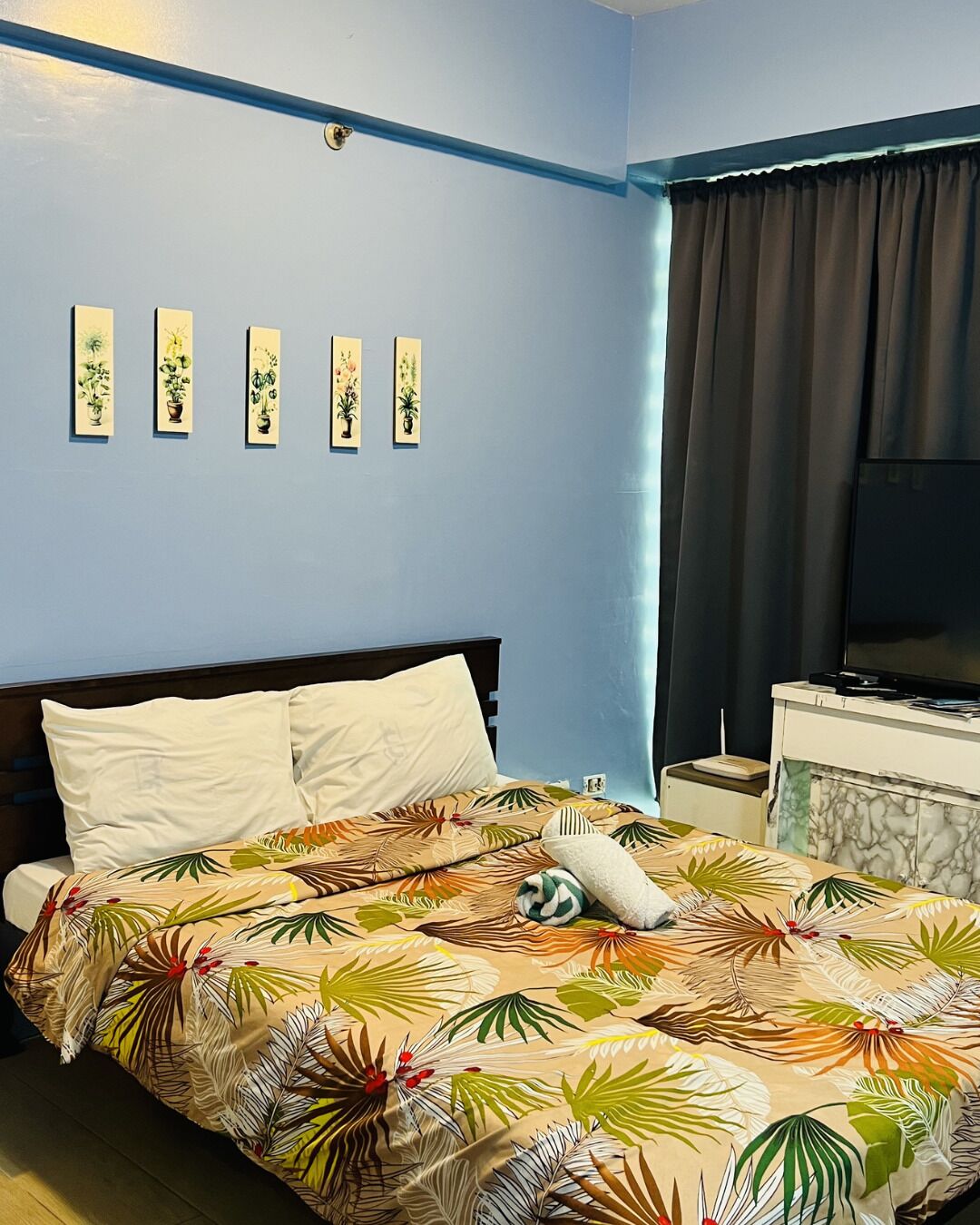 A hotel room with a bed, a TV, a nightstand, and a wall with framed pictures.