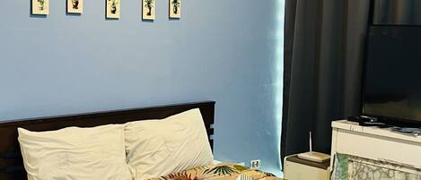 A hotel room with a bed, a TV, a nightstand, and a wall with framed pictures.