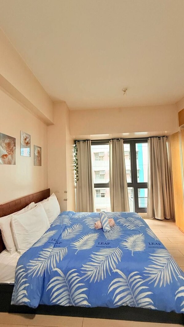 A hotel room with a large bed, a view of buildings through the window, and a ceiling fan. - HENRY & ADICHE  EMPERADOR BUILDING (Pasay)