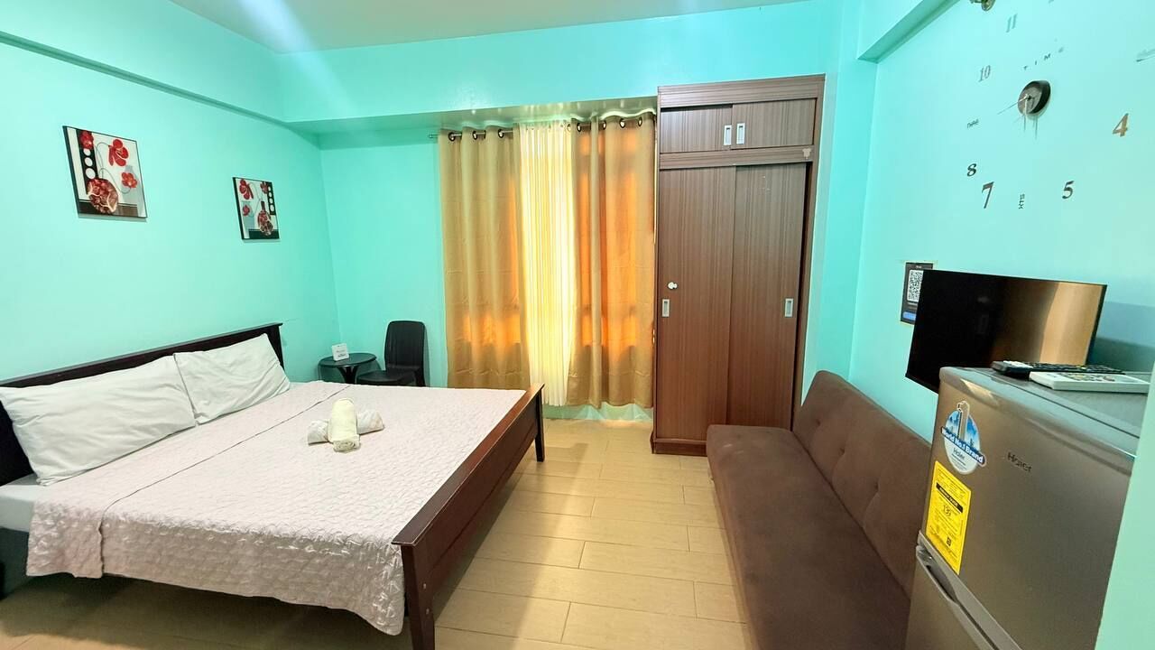Une chambre à coucher comprenant un lit, un canapé, un bureau avec un ordinateur, une armoire et une horloge murale.