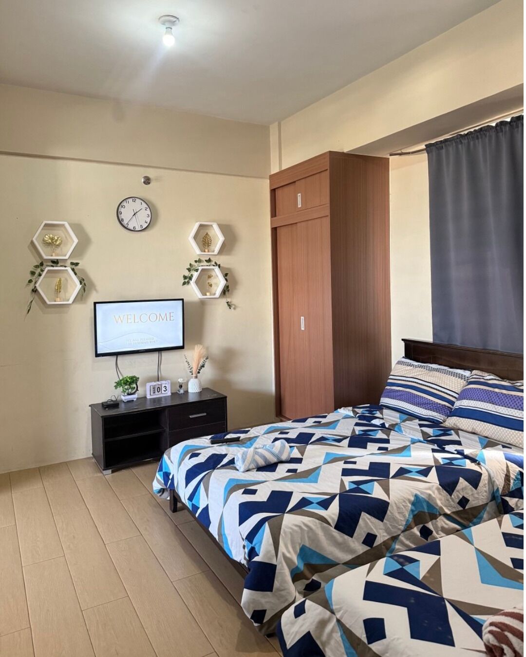Un dormitorio con cama, televisor, armario de madera y un reloj de pared.