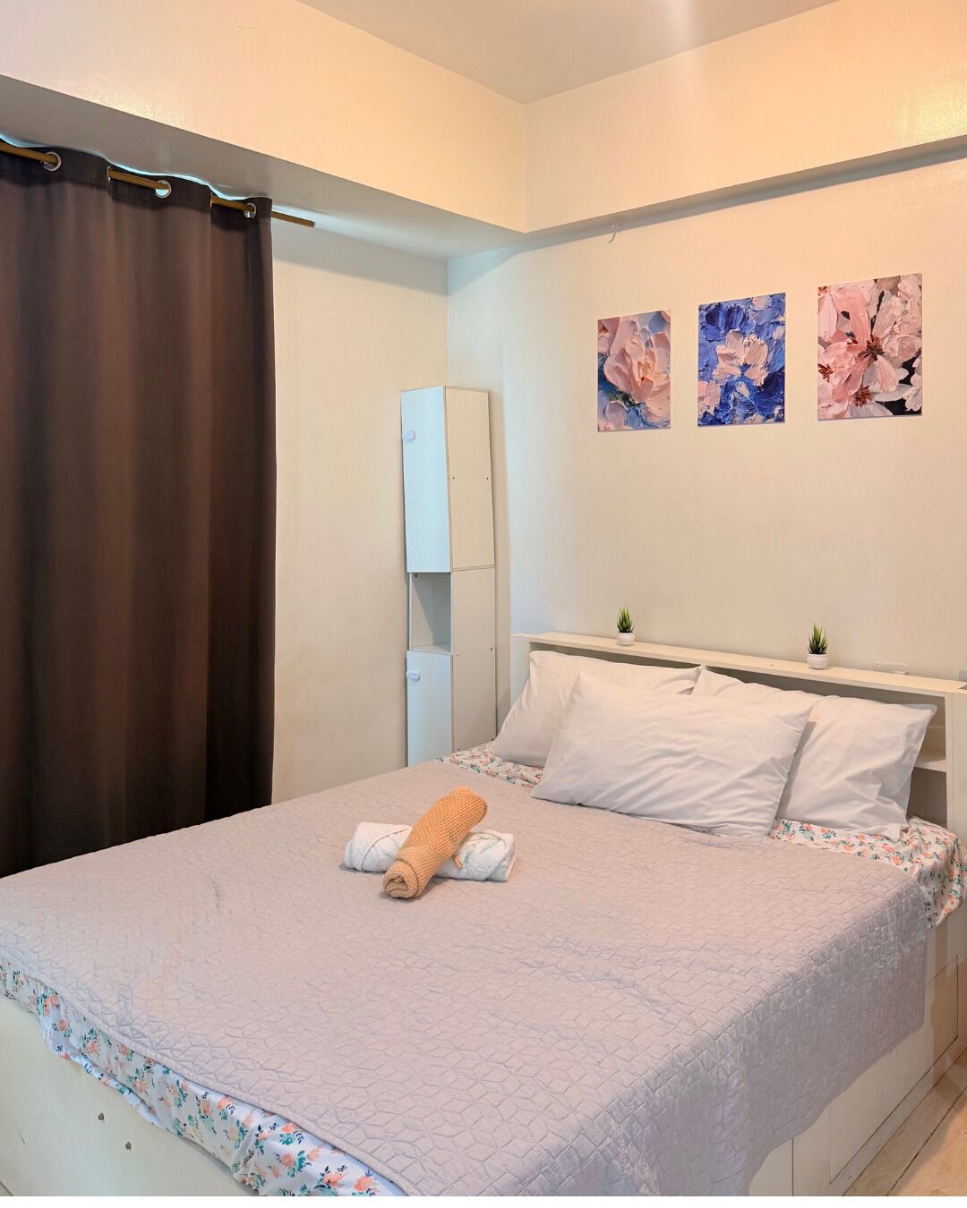 Een slaapkamer met een bed, een nachtkastje, een klein kastje en een wandplank.