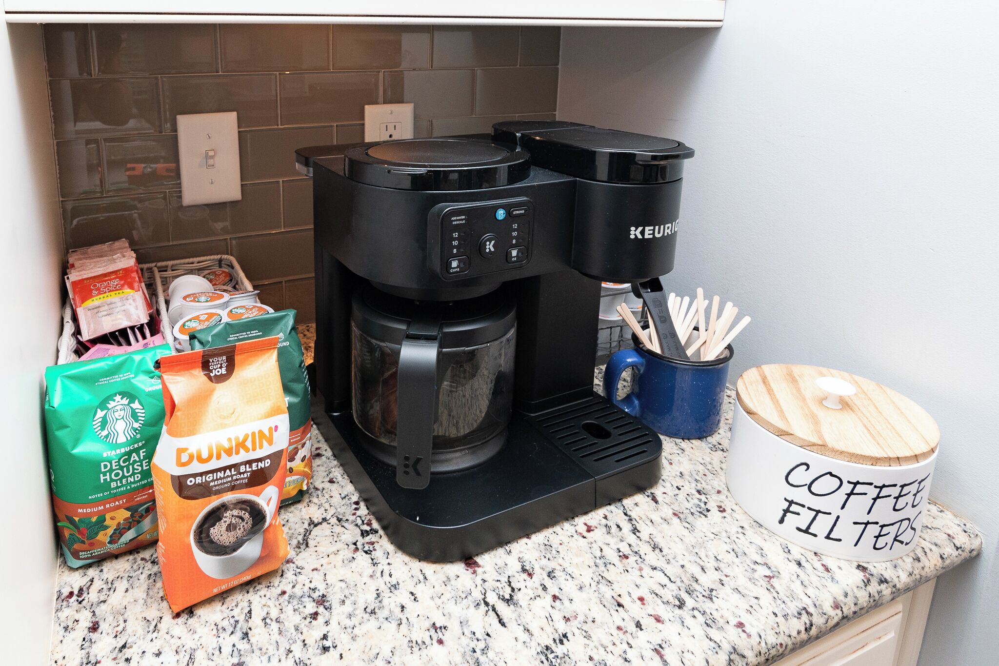 A coffee maker, Dunkin' coffee bags, and a coffee filter container on a kitchen counter.