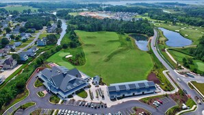 Vogelperspektive eines Golfplatzes mit Clubhaus, Parkplätzen und umgebenden Wohngebäuden.