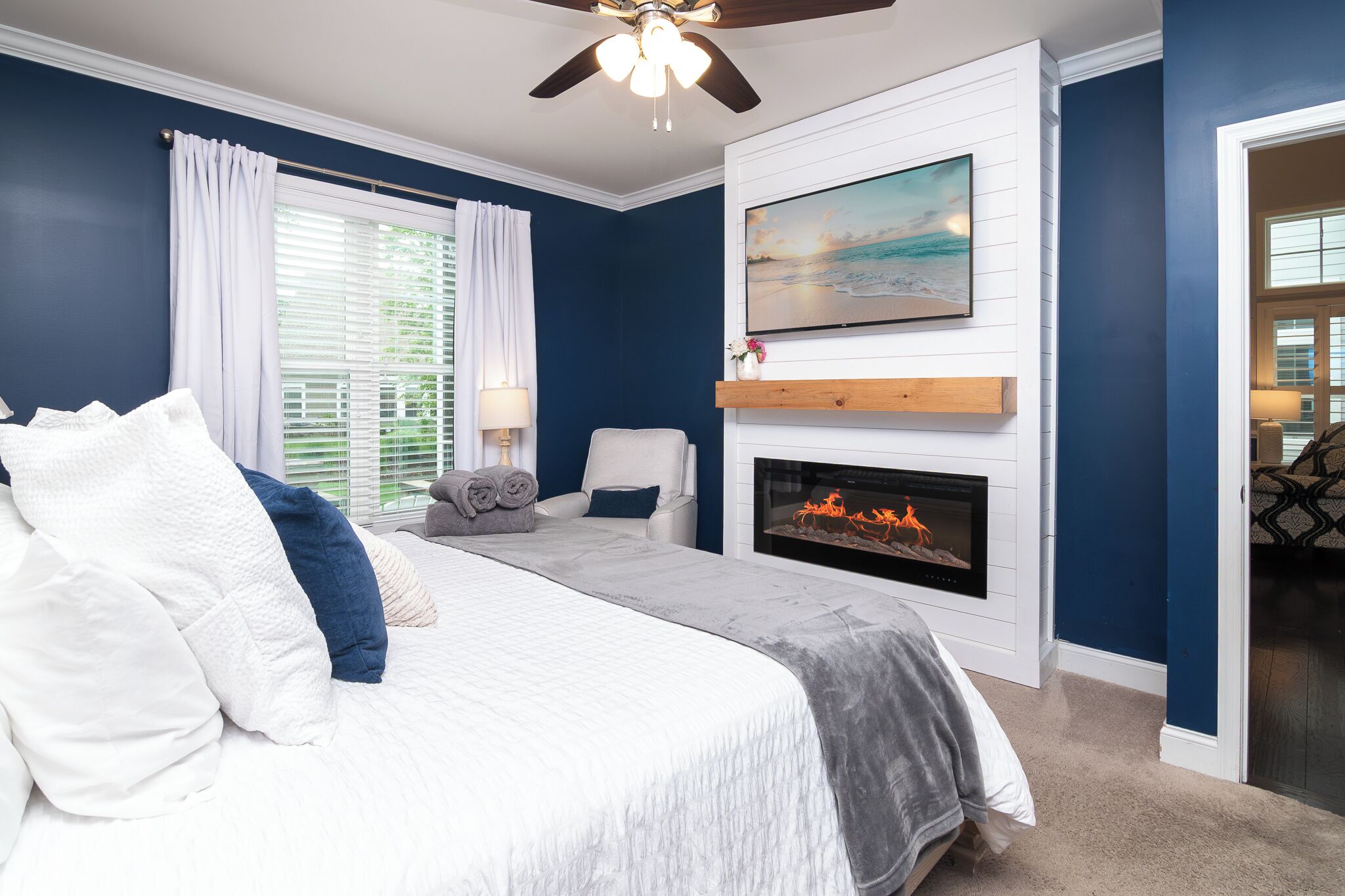 A bedroom with a bed, a fireplace, a ceiling fan, and a large window with curtains.