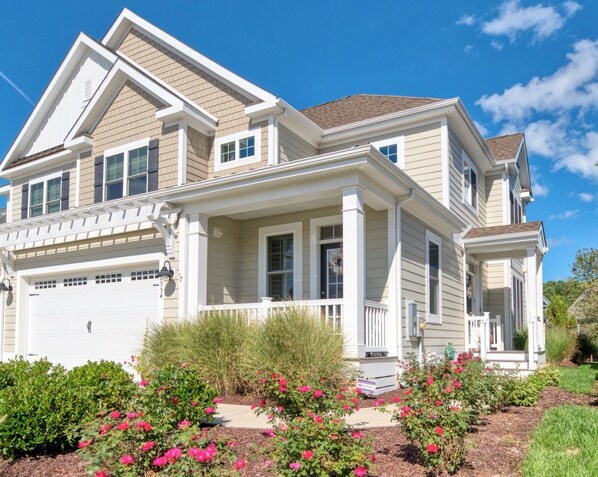 A two-story house with a front porch, garage, and a well-maintained garden with flowering plants.