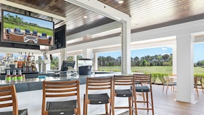 Eine Bar mit Fernseher, Holzstühlen und Blick auf einen Golfplatz.